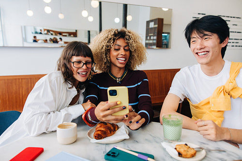 Friends laughing at phone in cafe together