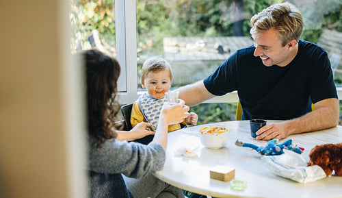 Parents feeding baby together at home