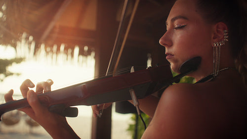 Young woman playing electric violin at sunset in a tropical resort