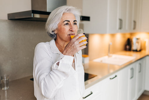 Elderly woman drinking a glass of fruit juice at home