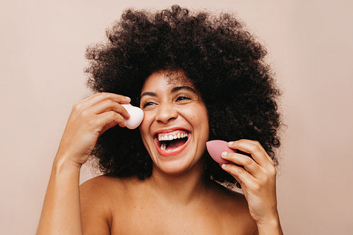 Beautiful young woman holding makeup sponges on her face