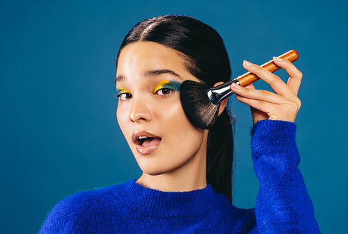 Woman applying foundation on her face using a makeup brush in a studio