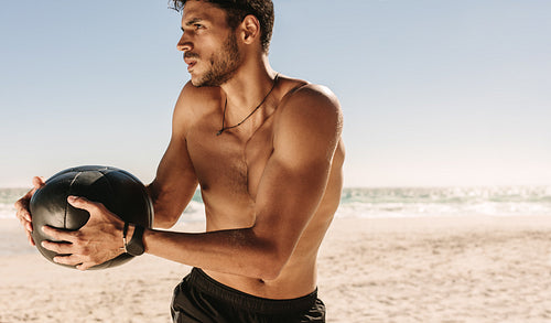 Man training at the beach using a medicine ball