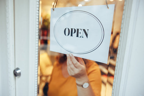 Woman hanging OPEN sign on store door 