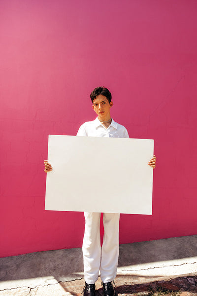 Assertive queer boy holding a white placard against a studio background