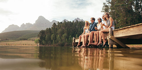 Friends sitting on pier at lake drinking beers