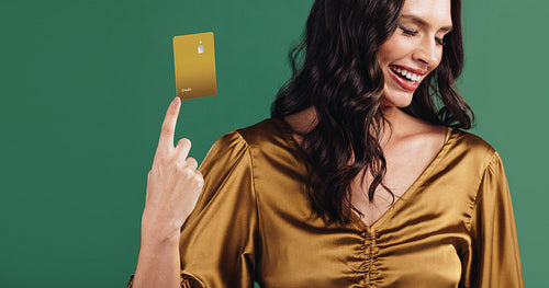 The fun future of payment: Happy woman holds up her gold credit card with her fingernail