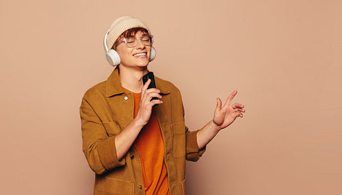 Happy man singing and dancing to music with smartphone and headphones on peach background