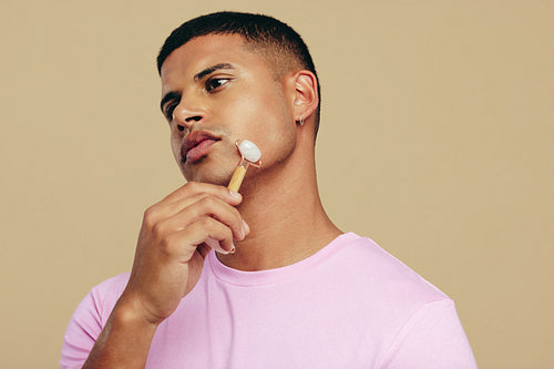 Youthful looking man using a jade roller on his face in a studio