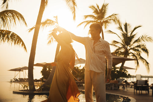 Romantic couple dancing poolside at sunset surrounded by palm trees