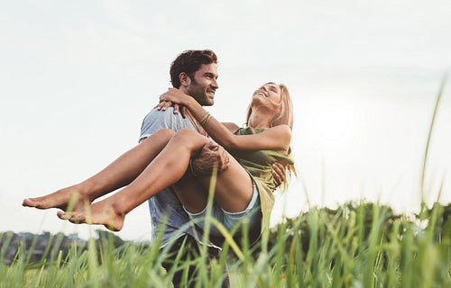 Young man carrying his girlfriend through a field