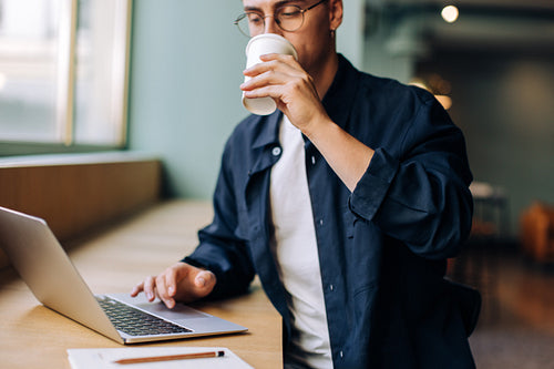 Young man in a cafe working on a laptop and drinking coffee