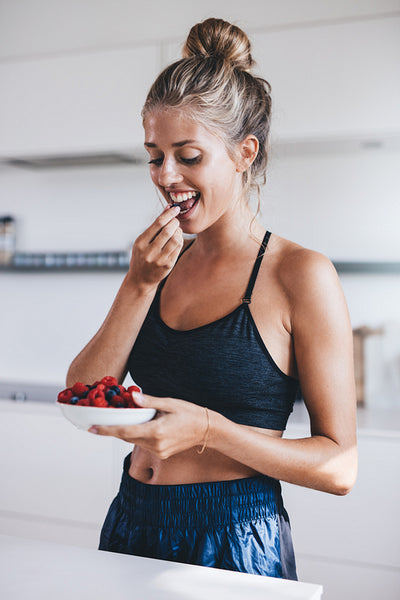 Beautiful young woman in kitchen eating berries