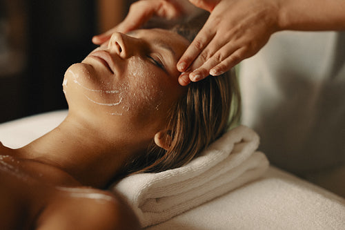Young woman receiving a facial spa treatment with exfoliation for skincare relaxation