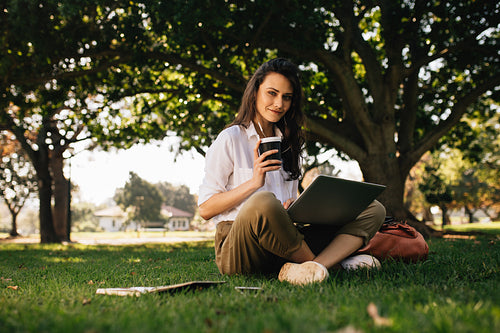 Beautiful woman sitting at park with a coffee and laptop