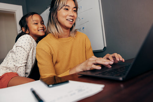 Happy little girl watching her mother work on a laptop