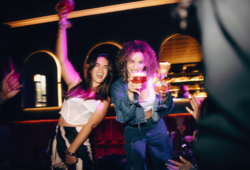 Two women celebrating with drinks in hand at a vibrant nightclub