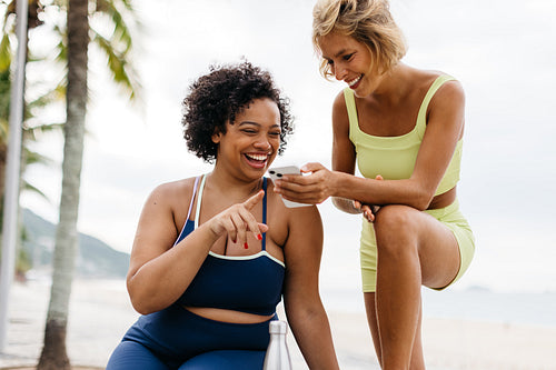 Two young women using a smartphone together on their workout break