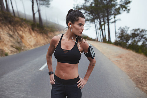 Confident young female athlete standing on country road 