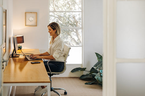 Happy young businesswoman working on a laptop in her office