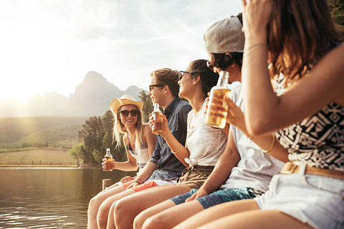 Young men and woman sitting on jetty with beers