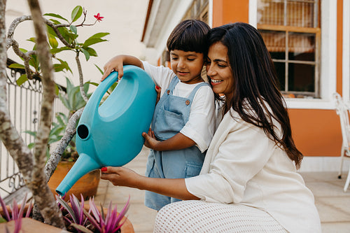 Mother and son watering plants together on a sunny balcony