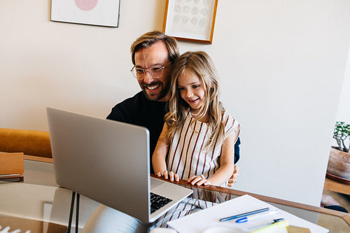 Father and daughter smiling at laptop during remote learning at home