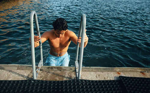 A sunny moment shows the man swimming up the dock ladder from the water.