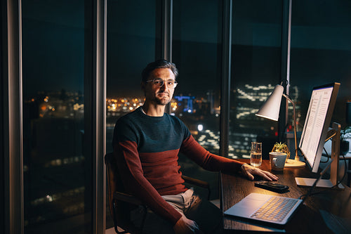 Entrepreneur working late: Businessman analyzing market research on his laptop and computer