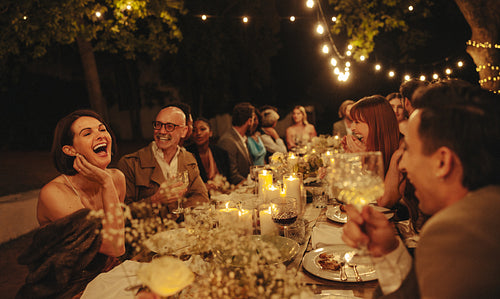 Friends laughing and celebrating at outdoor dinner party with string lights
