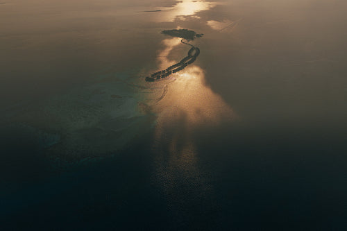 Aerial drone shot capturing stunning sunset over the Maldives, showcasing tropical islands, coral reefs, and serene ocean views