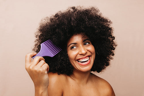 Gorgepus woman of color combing her natural hair in a studio