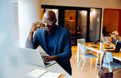 Businessman on a phone call working on a laptop in an office setting
