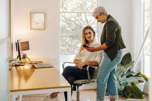 Businesswoman showing her colleague her smartphone screen