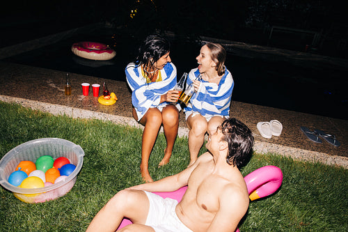 Friends by pool after dark enjoying drinks