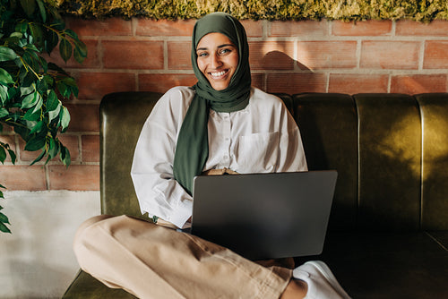 Happy woman with a hijab working on a laptop