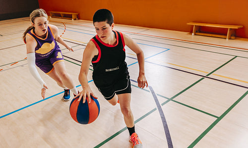 Two teenagers playing an intense basketball game on a hardwood court