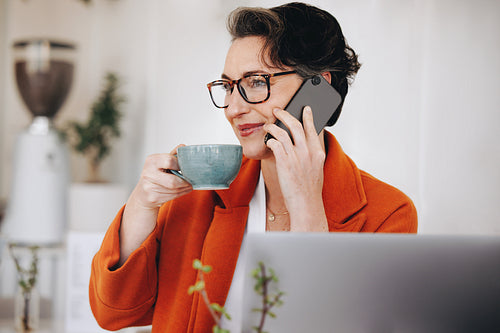 Businesswoman drinking coffee while taking a phone call in a cafe
