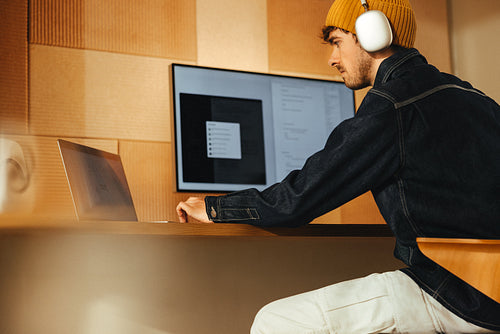Man works on a computer with headphones at a desk in a modern office