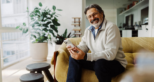 Senior man uses smartphone while relaxing on sofa at home