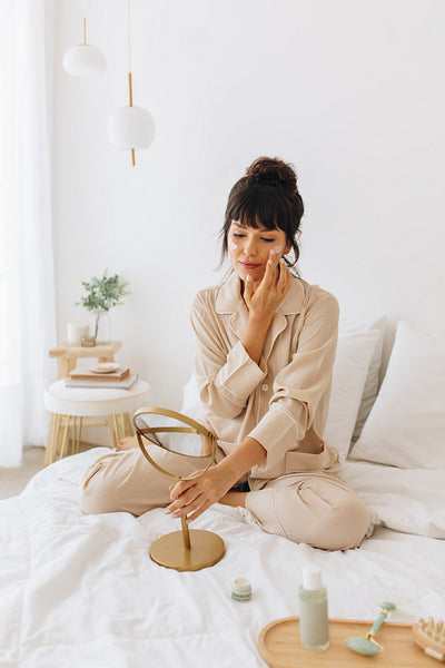 Young woman applying face cream sitting on bed