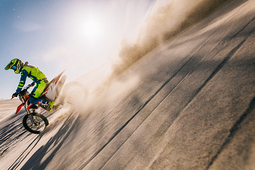 Professional motocross biker riding on sand dunes