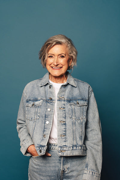Confident senior woman with a youthful smile standing in denim outfit on cheerful blue background