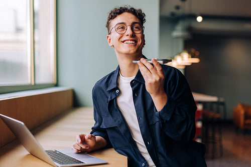 Young man recording a voice message while working at a desk with a laptop