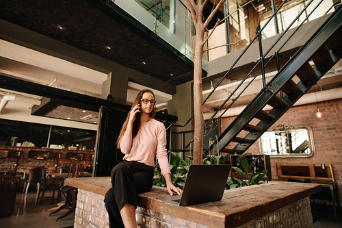 Creative woman in cafeteria with laptop and talking on phone