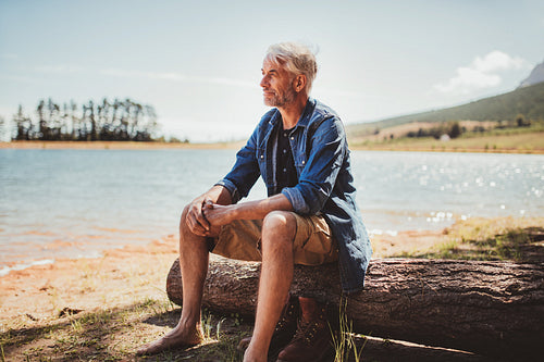 Mature man sitting on a log near lake