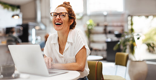 Happy woman doing freelance working using laptop in a coffee shop