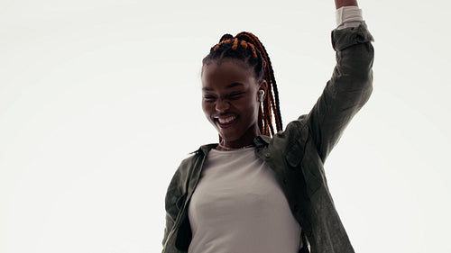 Young black woman with earbuds dancing to music, enjoying freedom and happiness in a studio