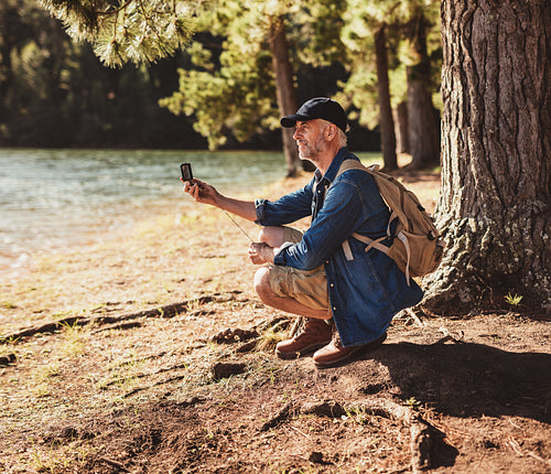 Senior man at a lake using compass for searching direction