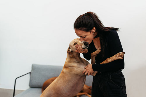 Affectionate young woman kissing her dog at home
